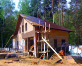 Фото на завершающем этапе строительства загородного дома с гаражом: стены построены, монтаж кровли выполнен, идет отделка